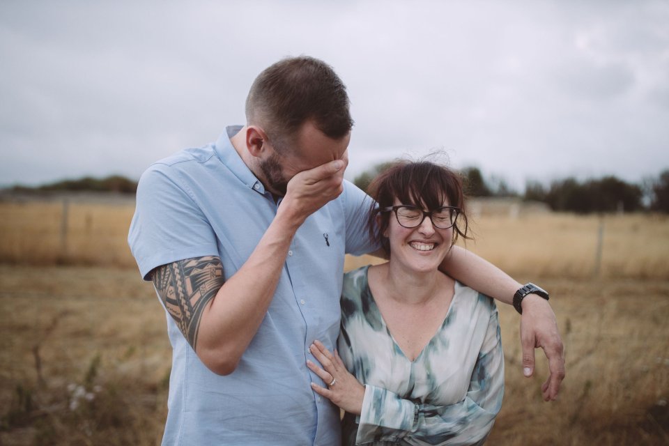 A couple sharing a happy, candid moment together in a grassy field.