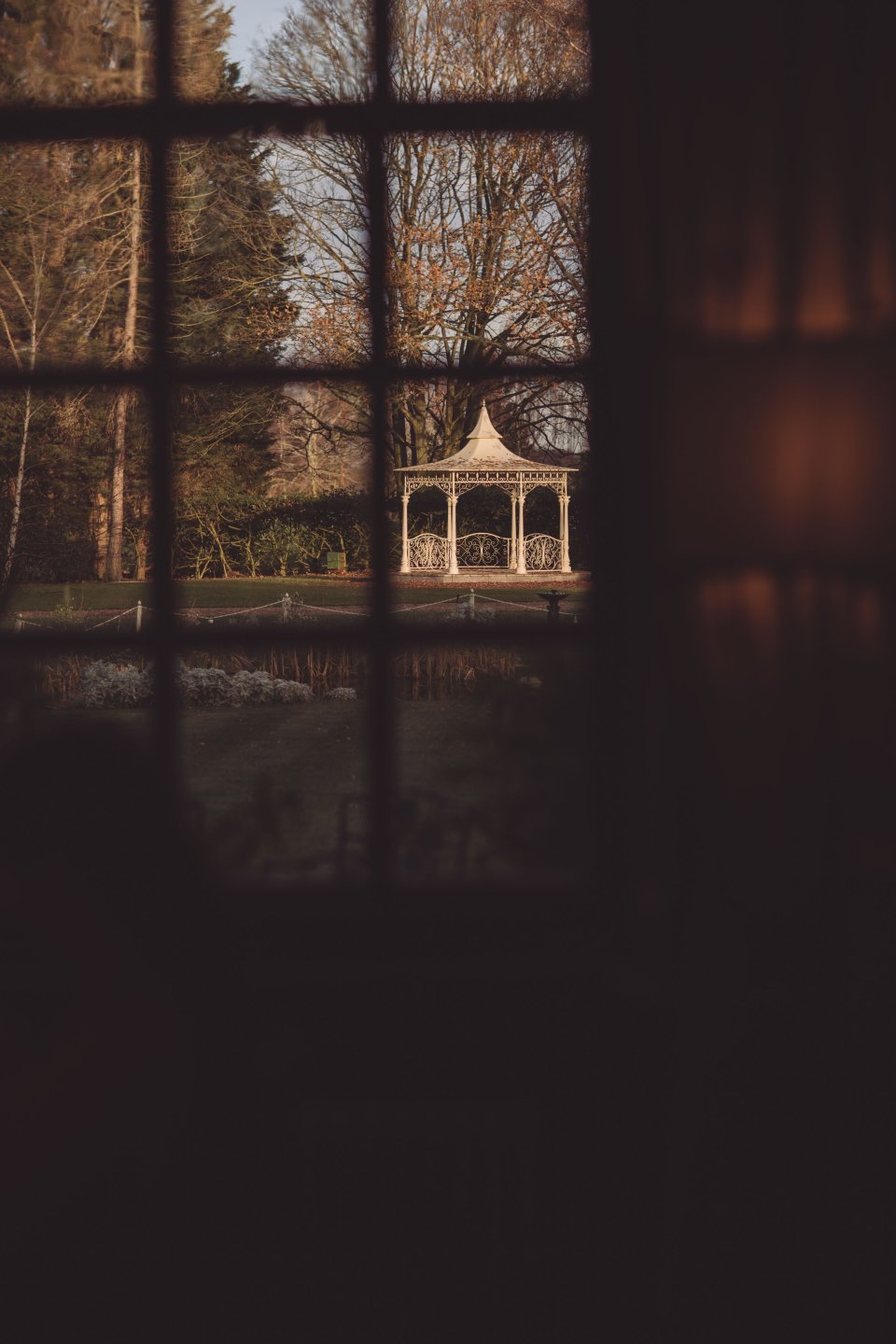 A bandstand in the back garden of Hintlesham Hall viewed through a window at sunset