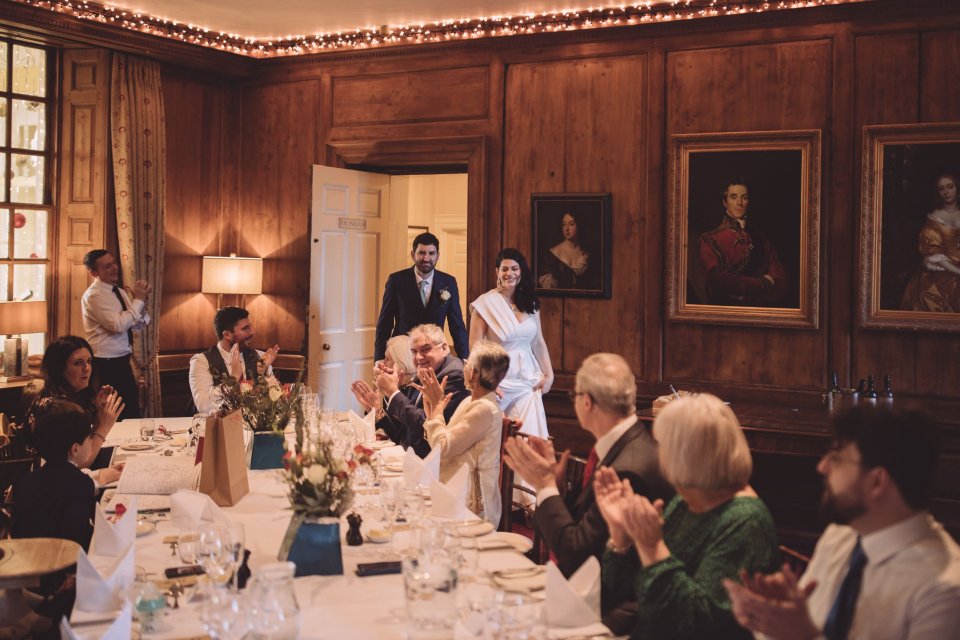 A bride and groom enter a wood panelled room at Hintlesham Hall for their wedding breakfast.