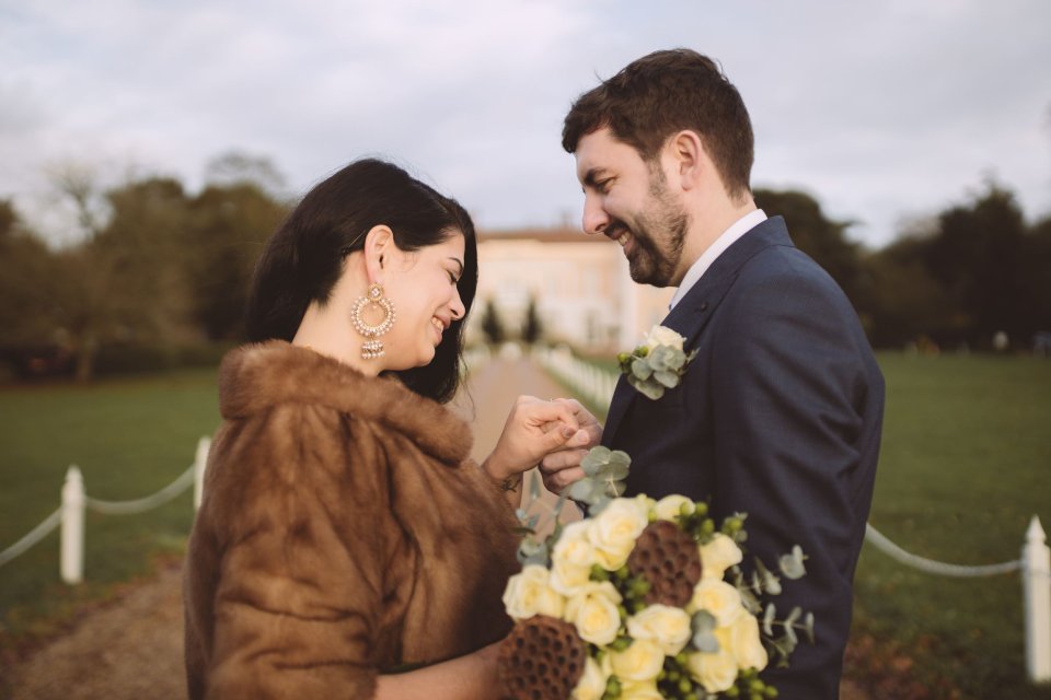 A bride and groom holding hands and smiling at each other outside Hintlesham Hall in Suffolk