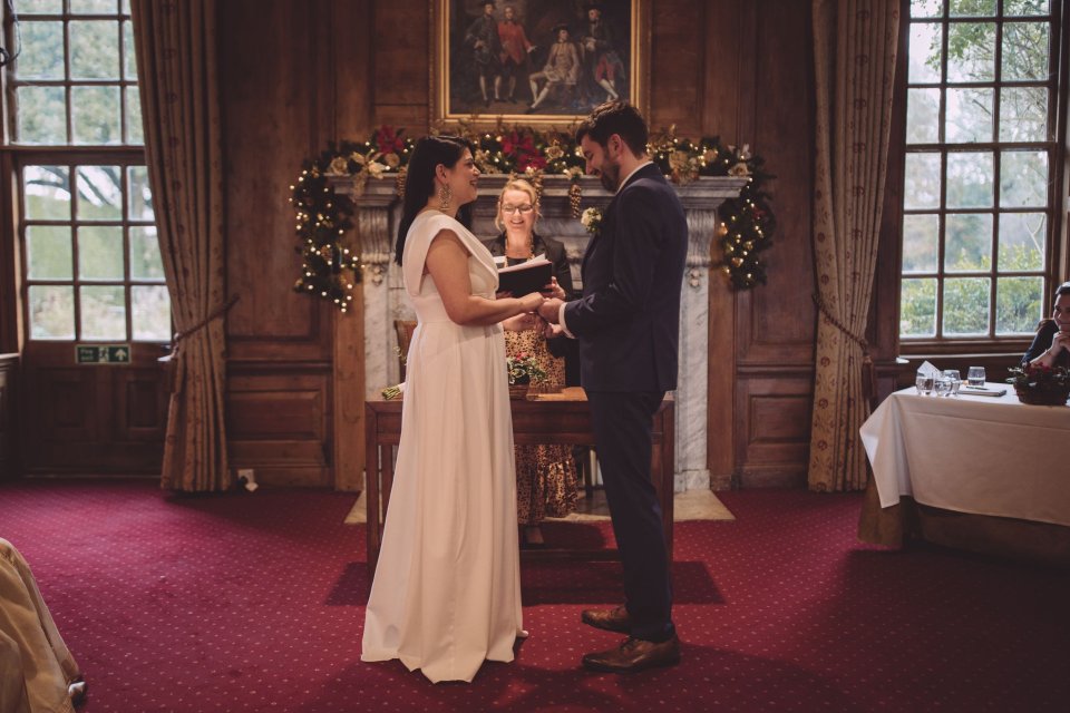 A bride and groom holding hands at the front of their Suffolk Hintlesham Halll wedding smile at each other