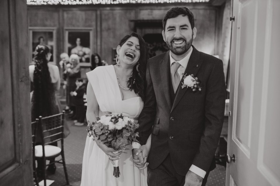 A bride and groom laugh as they exit their Hintlesham Hall ceremony holding hands