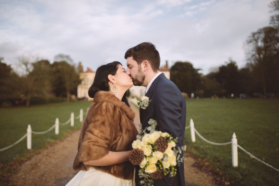 A bride and groom share a kiss outside the front of Suffolk Wedding Venue Hintlesham Hall