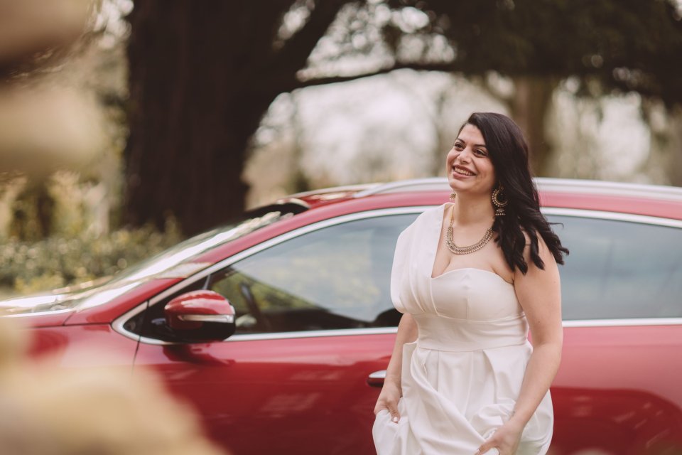 A bride arriving for her wedding at Hintlesham Hall with long dark hair exits a red car