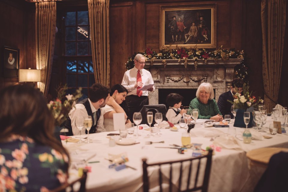 A father of the bride in a red tie stands at a table at Hintlesham hall to deliver a speech at a wedding