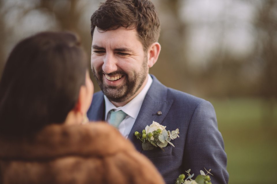 A groom wearing a green tie laughing as his wife looks up at him outside Hintlesham Hall in Suffolk