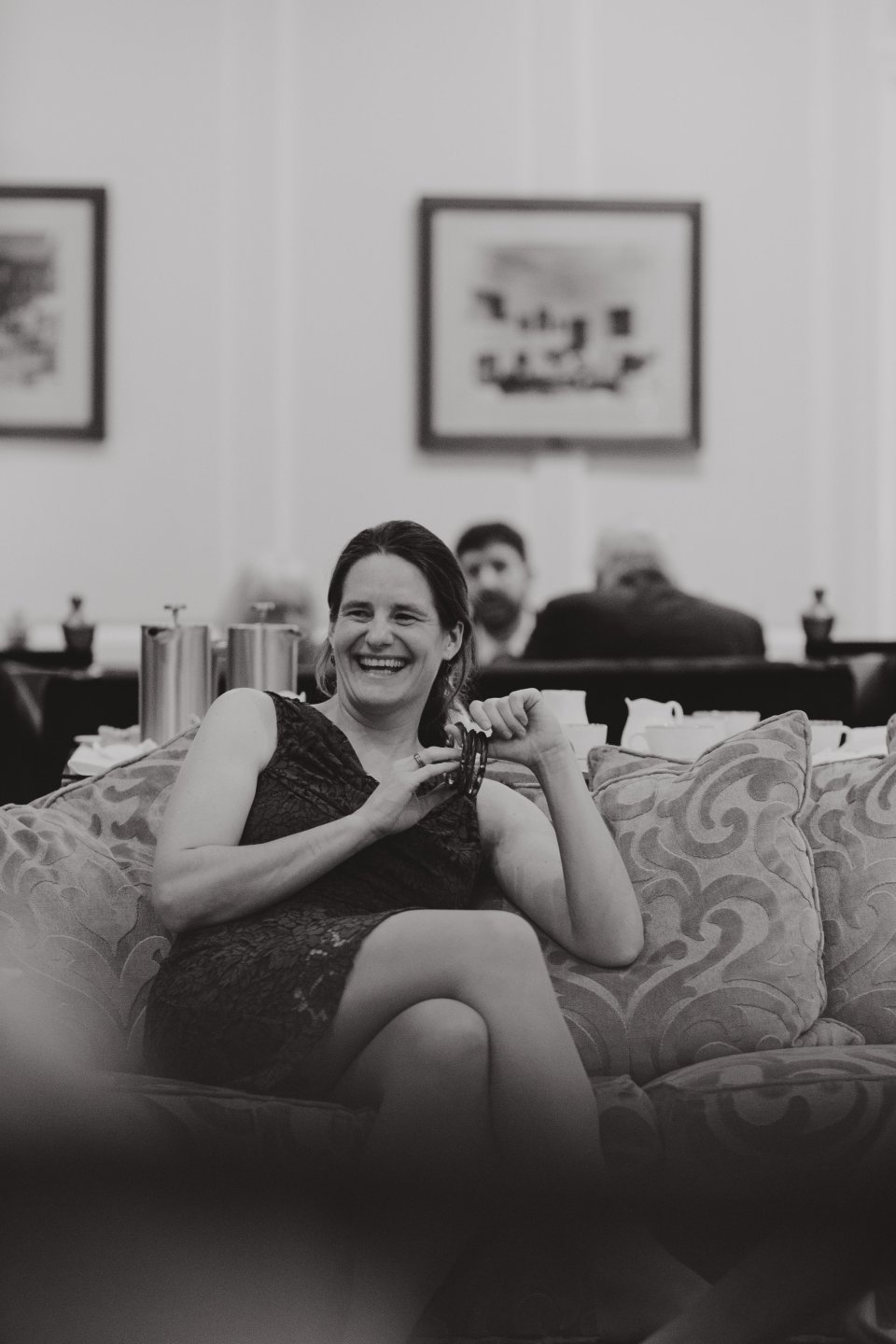 A woman laughs sitting on a sofa in a Hintlesham Hall drawing room during a wedding reception.