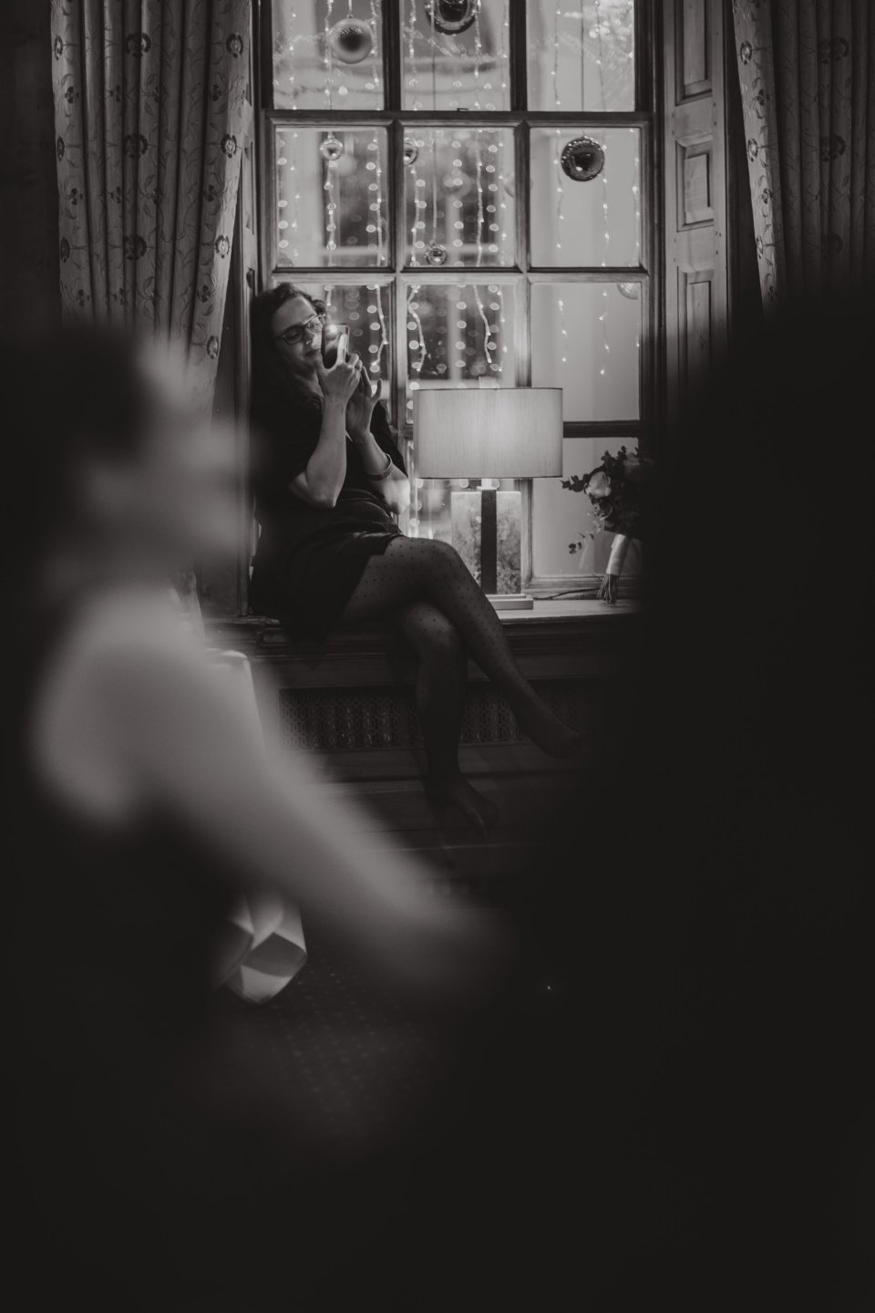 A woman sits on a window ledge and smiles as she videos speeches on her phone at Suffolk wedding venue Hintlesham Hall.