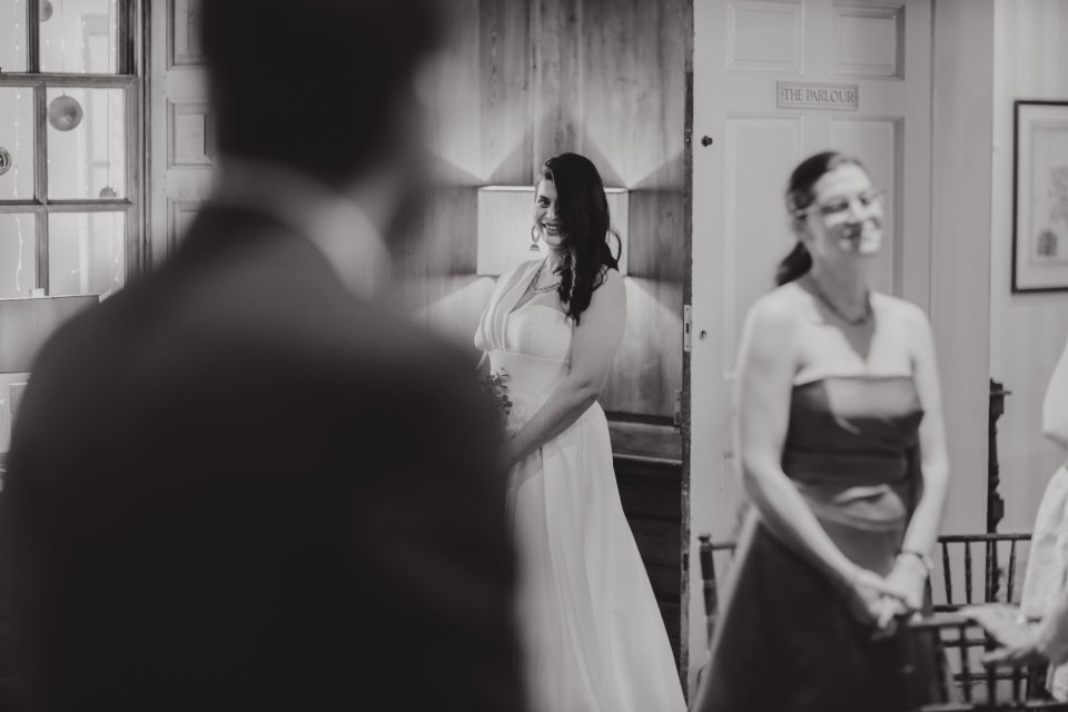 A young bride enters the ceremony room at her Hintlesham Hall wedding and she smiles towards her groom who is facing her
