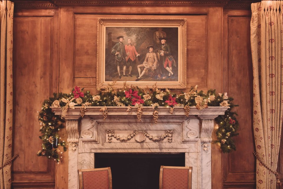 An ornate stone fireplace in Hintlesham Hall decorated with Christmas themed florist and a an oil painting hanging above