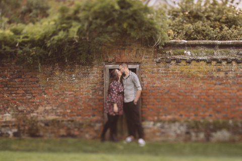 Couple standing close together against an aged brick wall in a garden setting.