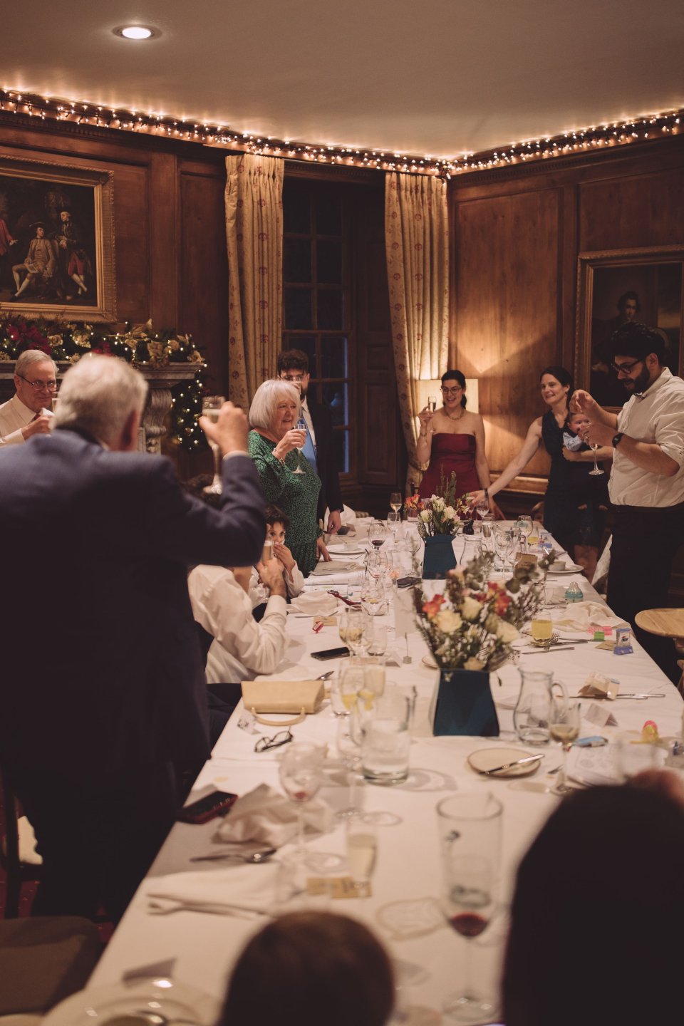 Guests stand round a table at a Hintlesham Hall wedding reception and raise a toast.