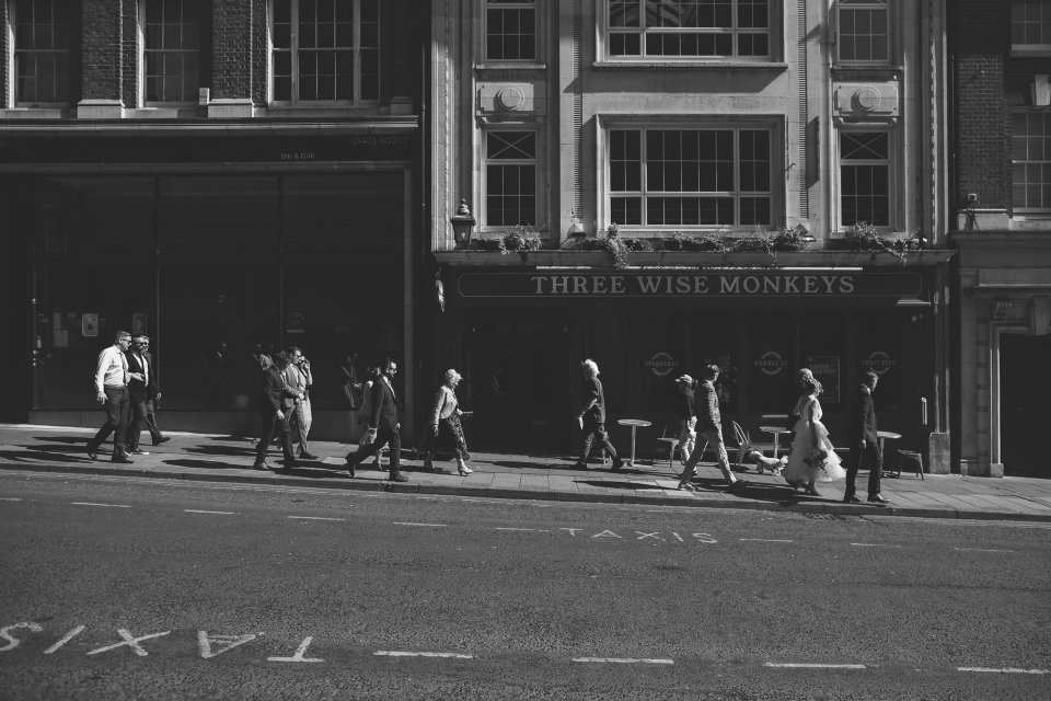 People walking on a busy urban street in front of storefronts in black and white photography.