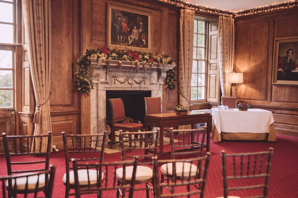 Suffolk wedding ceremony room in Hintlesham Hall with wood panelled walls, wooden chairs and an ornate fireplace