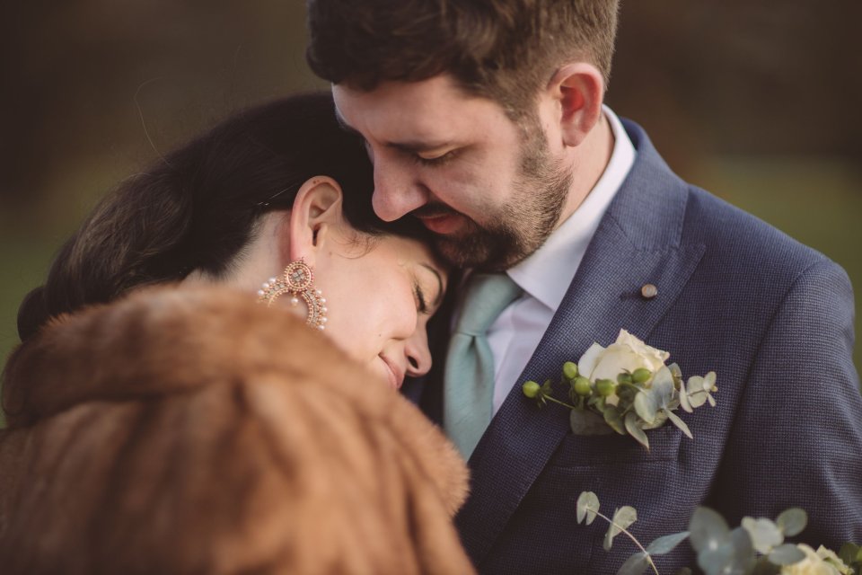 A bride rests her head on her groom's chest outside Hintlesham Hall in Suffolk
