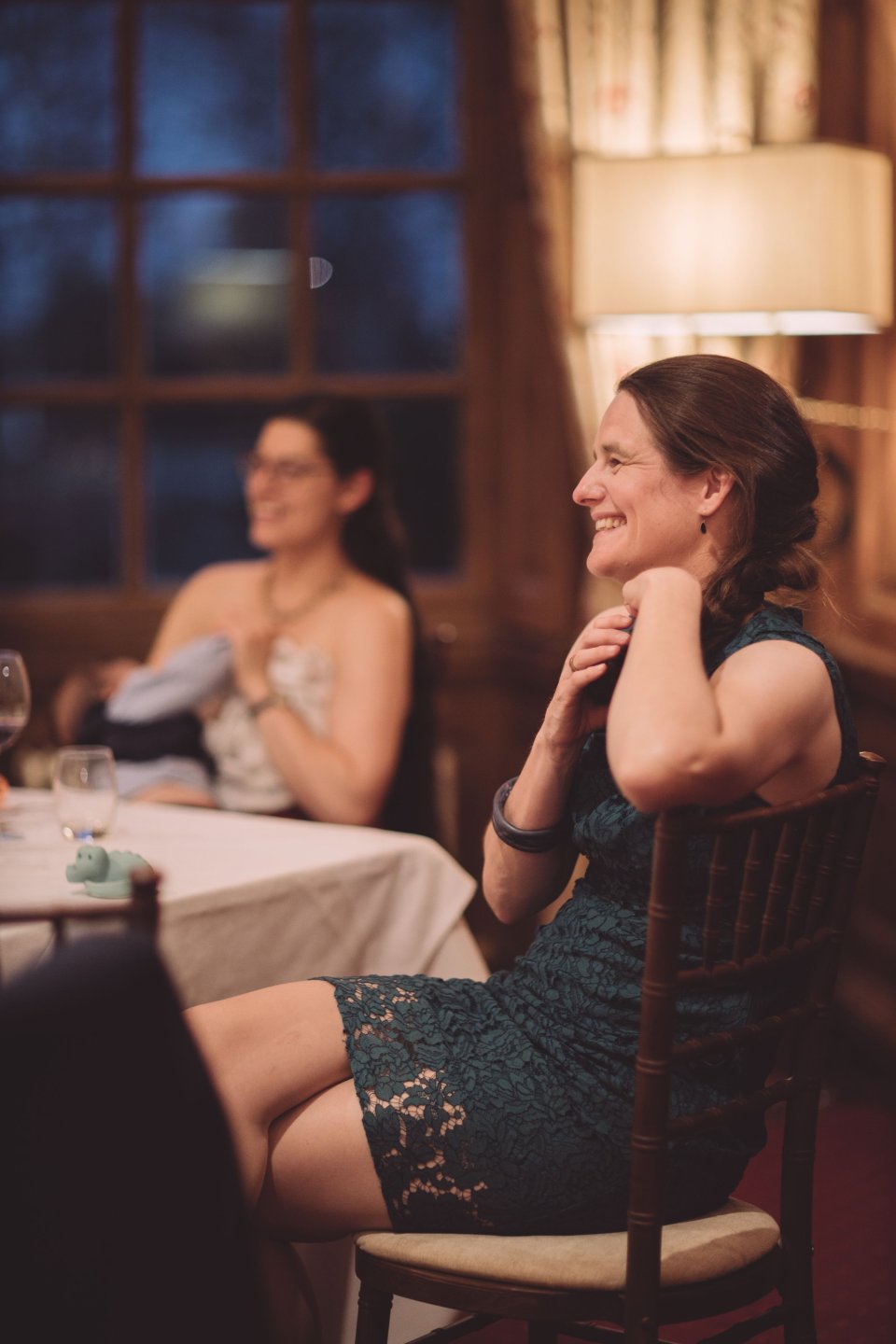 Two women laugh at a table at Hintlesham hall at a wedding reception during speeches.