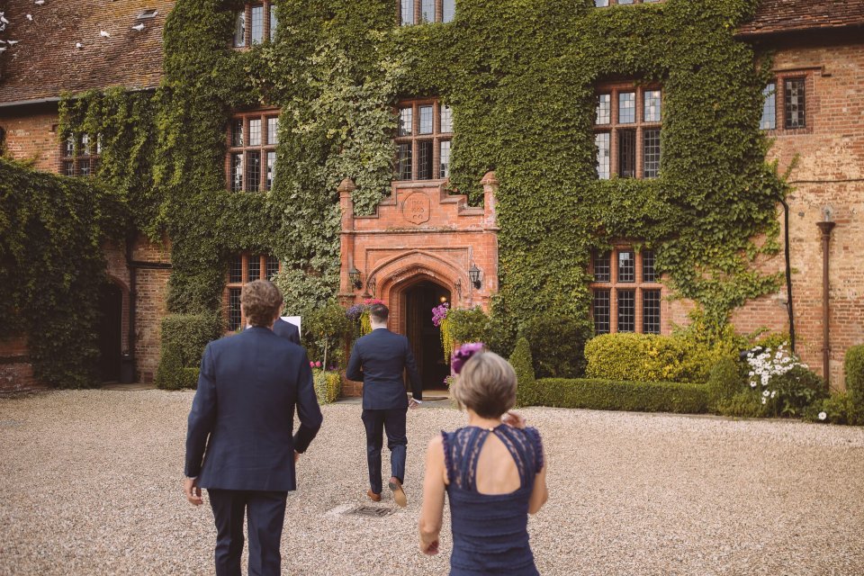 Wedding guests walking toward an ivy-covered brick mansion with  gravel driveway.