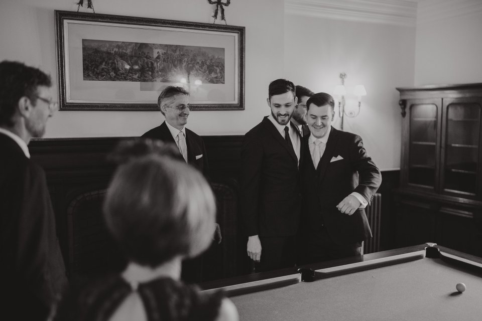 Black and white photo of groomsmen gathered around a billiards table in an elegant room.