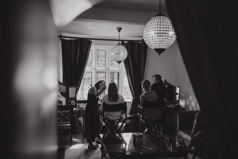 Black and white wide view of a bridal suite through a doorframe as a bridal party get ready for a wedding