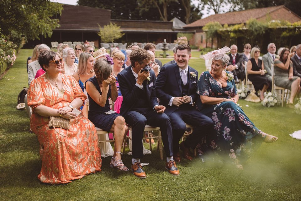 Tearful wedding guests in colourful attire seated on chairs during an outdoor ceremony.