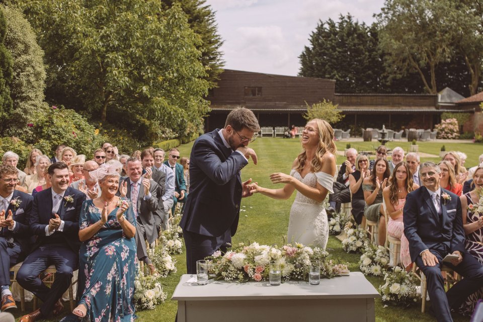 Couple celebrates during outdoor wedding ceremony surrounded by guests and floral decorations.