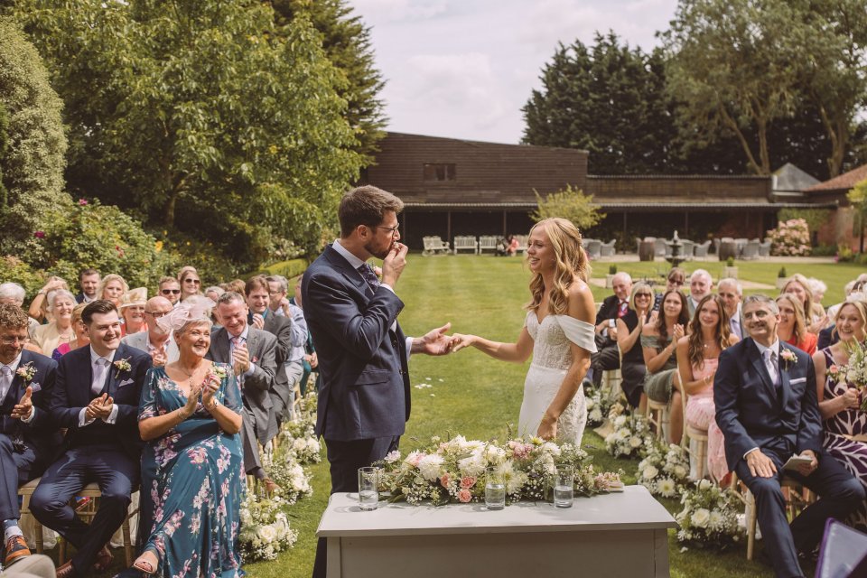 Joyful wedding celebration on lawn with guests watching and applauding.