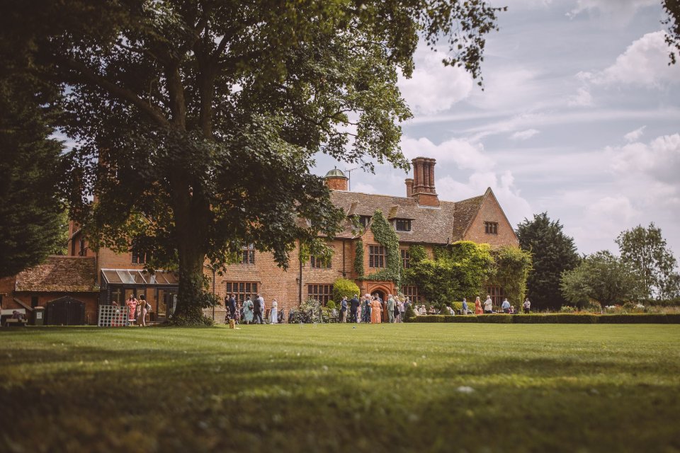 Rear view of Suffolk wedding venue Woodhall manor with guests gathering on lawn.