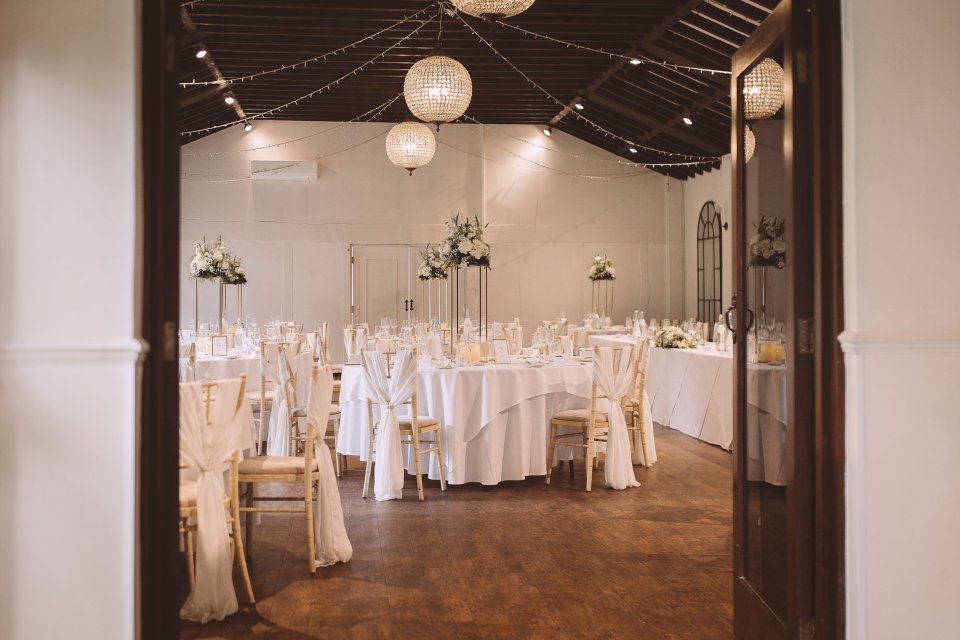 View of an elegant wedding reception setup through a doorframe with white-draped chairs and hanging lanterns.