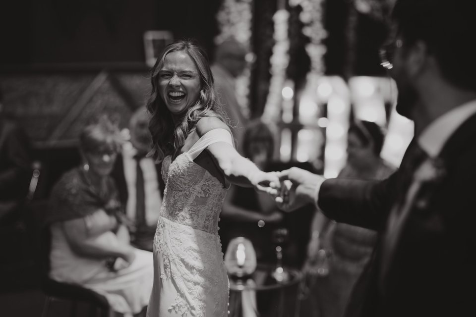 Black and white photo of joyful dancing at a wedding reception with hanging decorations visible.