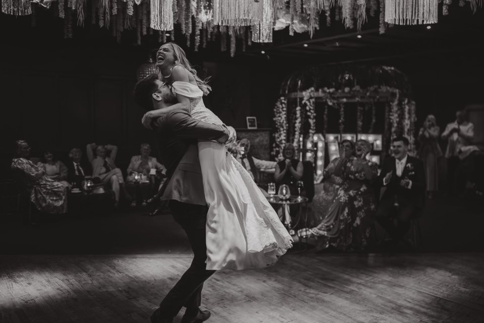 Black and white photo capturing a romantic dance lift moment at a wedding reception during first dance