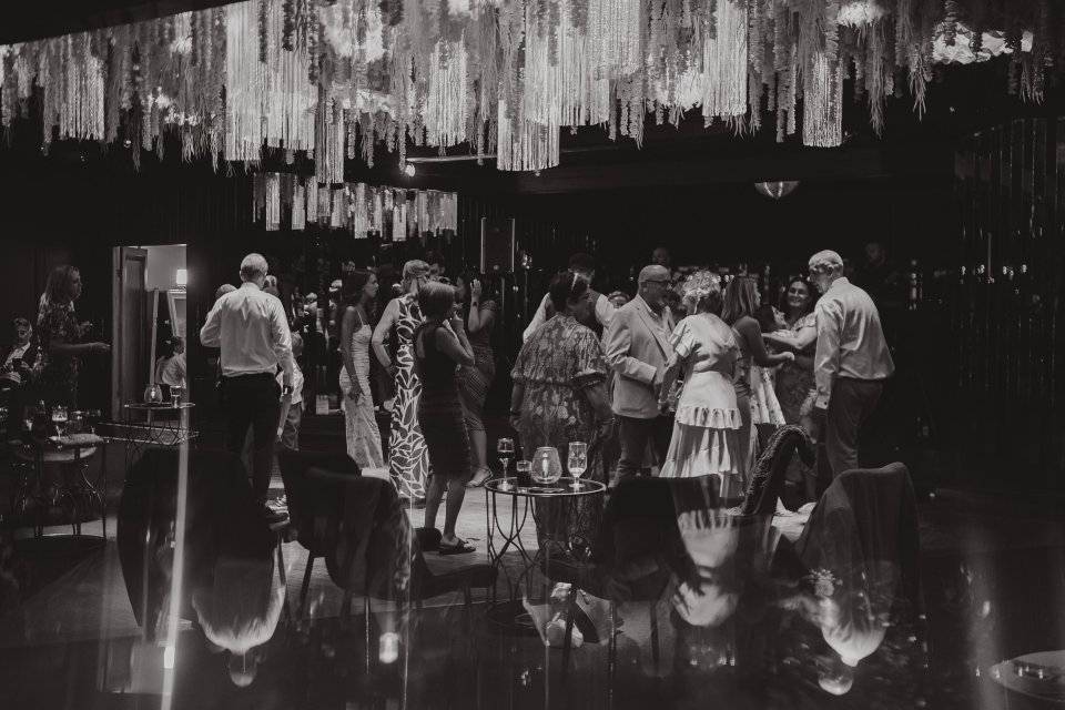 Black and white image of people dancing under decorative ceiling installations.