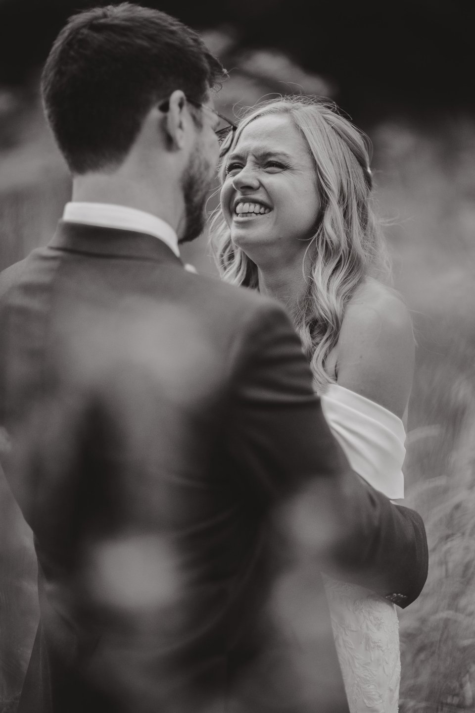 Black and white candid photo capturing a joyful moment between newlyweds outdoors.
