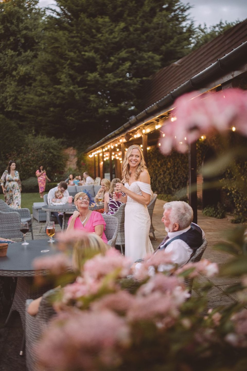 Outdoor wedding reception with string lights and pink flowers decorating a rustic venue.