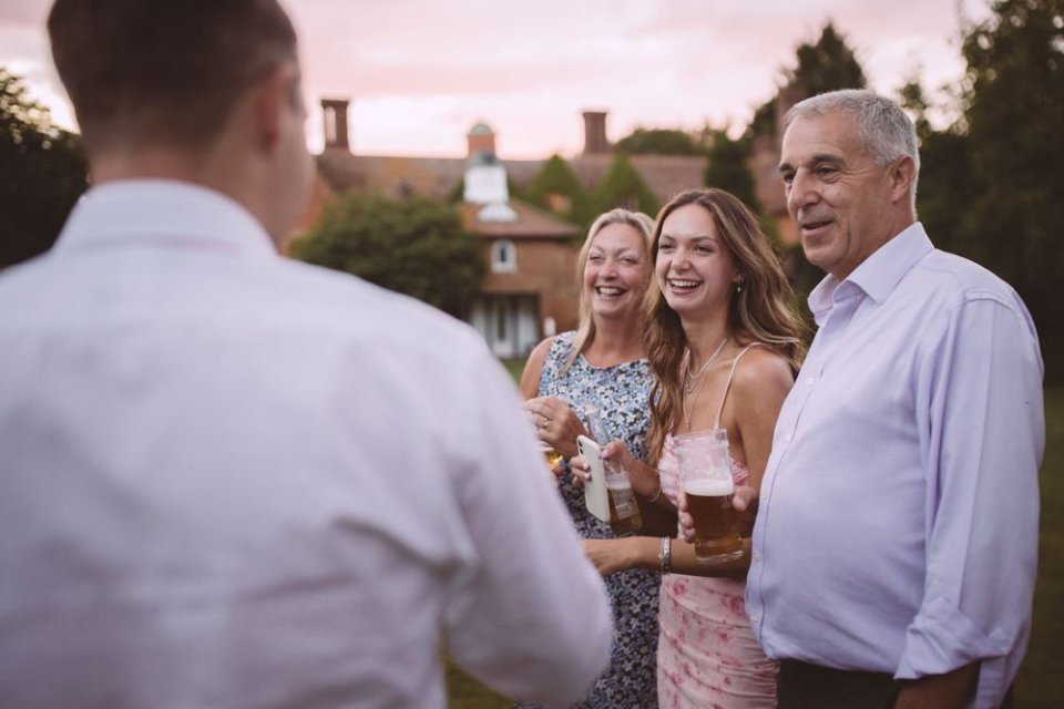 Candid moment during Suffolk wedding reception with guests enjoying drinks outdoors at sunset.