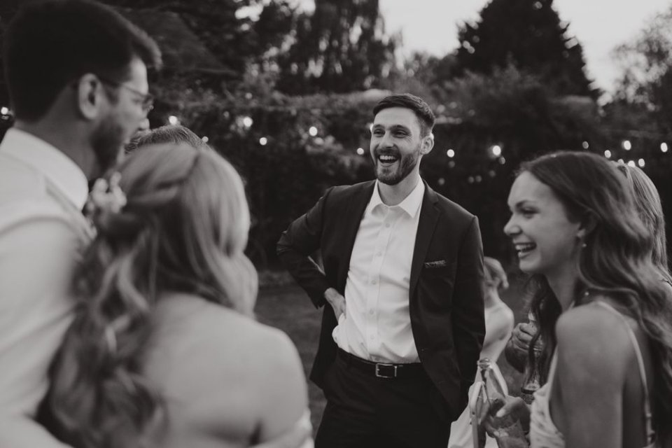 Black and white photo of wedding guests laughing together during an outdoor evening celebration.