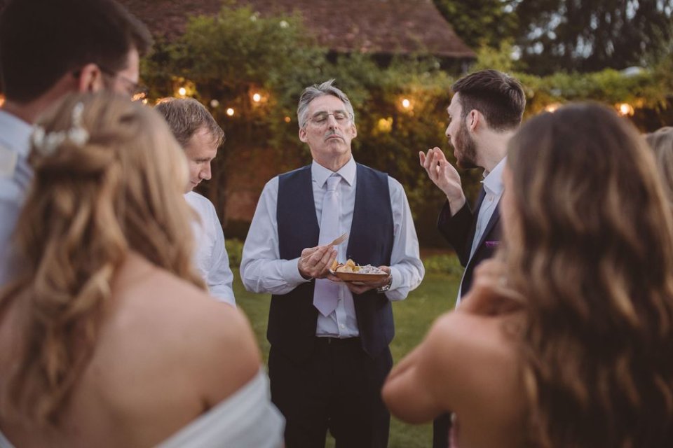 Wedding party gathered in a circle outdoors during evening reception with string lights.
