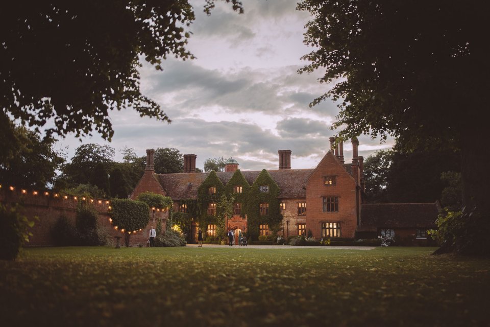 Historic Suffolk brick manor house illuminated at dusk with string lights hanging in the garden.