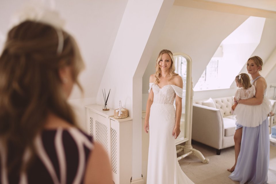 A bride smiles as she shows her wedding gown to her family in a stately bedroom